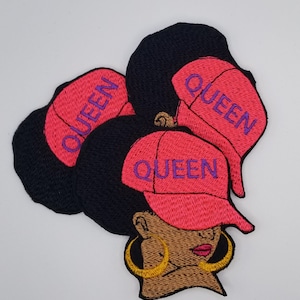 May include: Embroidered patch featuring a Black woman wearing a pink cap with the word "QUEEN" in purple. The woman has large gold hoop earrings and red lips. The patch has black hair.
