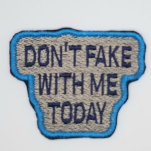 May include: Embroidered patch with the text "DON'T FAKE WITH ME TODAY" in navy blue thread. The patch has a light gray background with a blue border, and a unique shape.