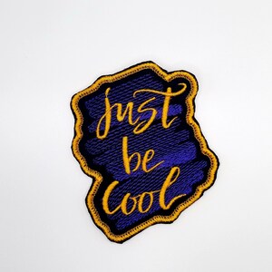 May include: Purple and gold embroidered patch with the text "Just be cool" in a stylized font.