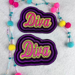 May include: Two embroidered patches with the word "Diva" in pink script with a neon green outline, set against a black background and a purple cloud-like border. A beaded necklace with colorful pom-poms and beads is also present.
