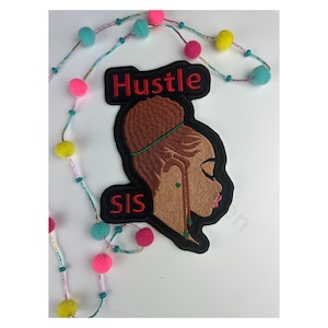 May include: An embroidered patch featuring a profile of a woman with the words "Hustle SIS" in red and black. The woman has brown skin, a bun, and green earrings. A beaded garland with pink, yellow, and teal pom-poms is in the background.