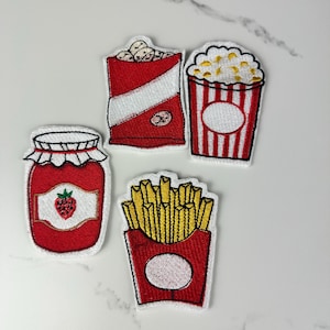 May include: Embroidered patches featuring food items: a jar of jam with a strawberry, a bag of popcorn, a popcorn container, and a container of french fries. Each patch has a white border and is set against a white background.