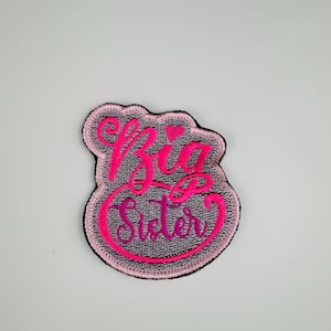 May include: Pink and purple embroidered patch with the text "Big Sister" in a cursive font.