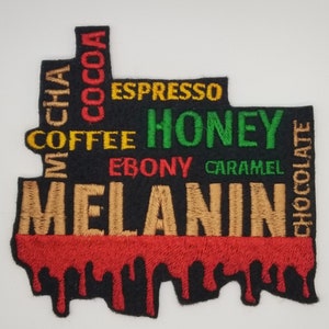May include: Black embroidered patch with the word "MELANIN" in gold thread. The word is surrounded by other words in different colors, including "mocha", "cocoa", "coffee", "espresso", "honey", "ebony", "caramel", and "chocolate".