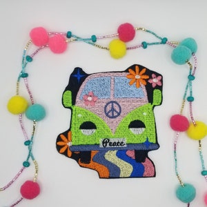 May include: Green and pink embroidered patch of a vintage van with a peace sign and the word "Peace" on the front. The van is driving on a rainbow road with stars and flowers.