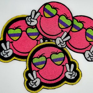 May include: Three pink smiley face patches with yellow outlines and green, purple, and yellow sunglasses. Each patch has two white peace signs.