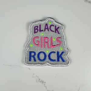 May include: A gray embroidered patch with the words "BLACK GIRLS ROCK" in purple, pink, and blue. The patch has a silver border and small green star accents.