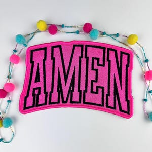 May include: Pink fabric patch with black embroidered letters spelling "AMEN".