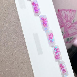 May include: A set of white, glittery, rectangular stickers with pink text. The stickers are labeled with the months of the year: January, February, March, April, May, June.