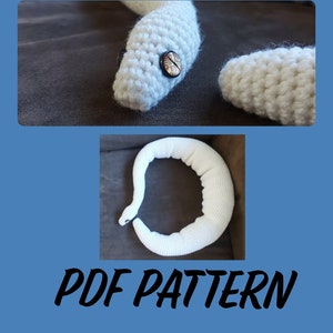 Pode incluir: Uma cobra branca de crochê com um olho de botão. A cobra é mostrada em duas vistas, uma com a cabeça e um olho de botão, e a outra mostrando o corpo. O texto "PDF PATTERN" está escrito em itálico preto.