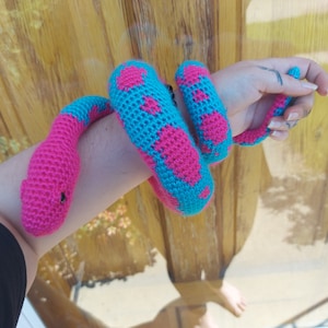May include: A crocheted snake toy with pink and blue yarn. The snake is curled up on a person's arm.