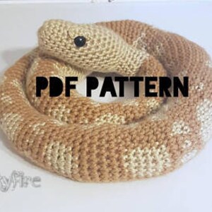 May include: A knitted snake toy in shades of tan and cream, coiled on a white surface. The snake has a detailed pattern and a black eye. The text "PDF PATTERN" is displayed in black. The word "Skyfire" is also visible.