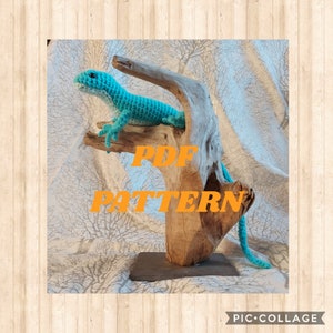 Op de afbeelding: Een turquoise gehaakte hagedis die op een stuk drijfhout zit. Het drijfhout staat op een zwarte leisteen basis. De tekst "PDF PATTERN" is in oranje letters op het drijfhout geschreven.