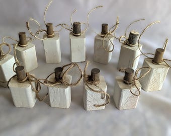 May include: A collection of ten small, white, rectangular wooden blocks, each topped with a brown, cylindrical piece and tied with twine. The blocks are arranged on a white surface, suggesting a craft or decorative item.