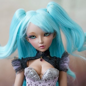 Puede incluir: Una mu&ntilde;eca con el pelo largo y azul brillante peinado en coletas. La mu&ntilde;eca lleva un vestido negro y plateado con un corpi&ntilde;o de encaje y un collar oscuro con una piedra preciosa p&uacute;rpura.