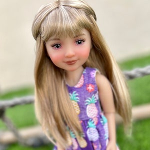 May include: A doll with long blonde hair wearing a purple dress with a pineapple print.