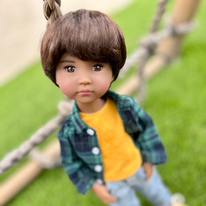 May include: A doll with brown hair wearing a green and black plaid shirt over a yellow t-shirt, blue jeans, and white sneakers.
