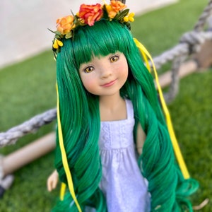 May include: A doll with long, green hair and a flower crown. She is wearing a white dress and has yellow ribbons in her hair.