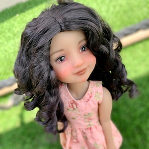 May include: A doll with long, dark curly hair wearing a pink floral dress. The doll has rosy cheeks and brown eyes.