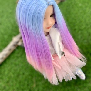 May include: A doll with long, ombre hair that transitions from light blue to purple to pink. The doll is wearing a white jacket, a pink tulle skirt, and white shoes.