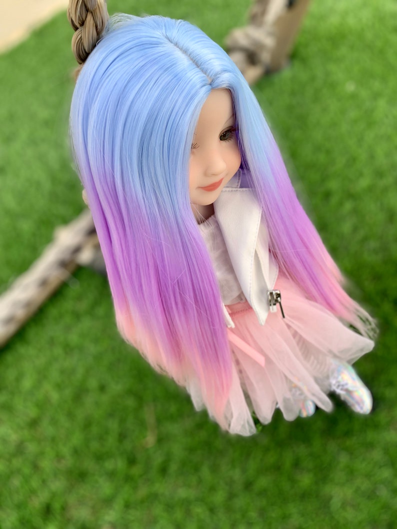 May include: A doll with long, ombre hair that transitions from light blue to purple to pink. The doll is wearing a white jacket, a pink tulle skirt, and white shoes.