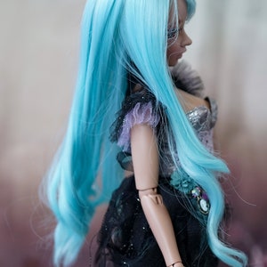 Puede incluir: Una mu&ntilde;eca con el pelo largo, suelto y azul turquesa. La mu&ntilde;eca lleva un vestido negro y plateado con detalles de encaje. La cara de la mu&ntilde;eca est&aacute; parcialmente oculta por el pelo.