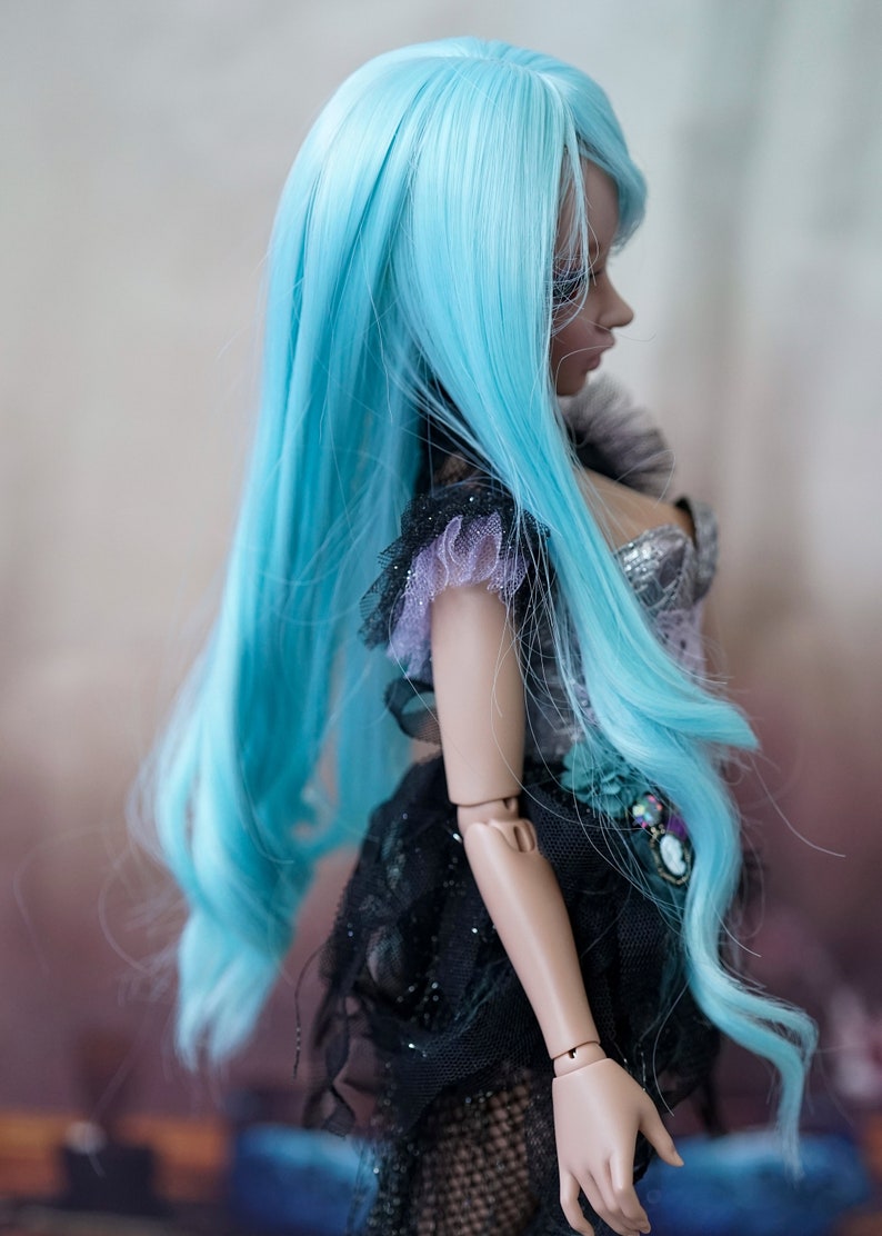 Puede incluir: Una mu&ntilde;eca con el pelo largo, suelto y azul turquesa. La mu&ntilde;eca lleva un vestido negro y plateado con detalles de encaje. La cara de la mu&ntilde;eca est&aacute; parcialmente oculta por el pelo.