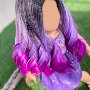 May include: A doll with a wig featuring a dark to light purple ombre. The wig has long, wavy curls with a vibrant magenta at the tips. The doll is wearing a purple dress with gold star accents.