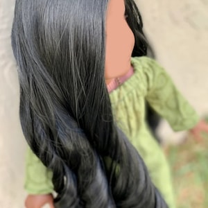 May include: A doll with long, black, wavy hair wearing a green dress.