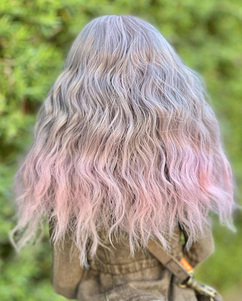 May include: A doll with long, wavy hair. The hair is a blend of gray and silver at the roots, transitioning to a soft pink at the ends. The doll is wearing a brown jacket with a strap across the chest.