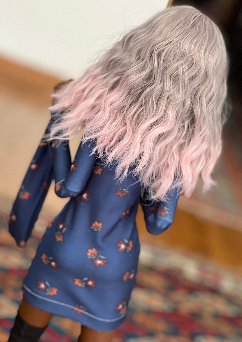 May include: A navy blue dress with a floral pattern in shades of orange and red. The dress has long sleeves and a rounded neckline. The model is wearing a wig with wavy gray hair that fades to pink at the ends. The model is also wearing black boots.