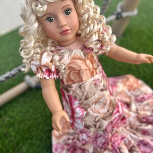 May include: A doll with blonde curly hair wearing a pink and brown floral dress.