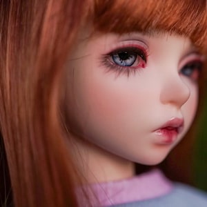 May include: A close-up of a doll's face with red eyeshadow, long eyelashes, and blue eyes. The doll has long, straight, red hair.