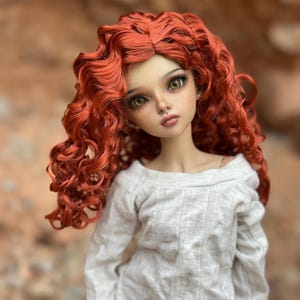 May include: A doll with long, curly, red hair wearing a white, ribbed, long-sleeved shirt.