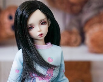 May include: A doll with long black hair wearing a light blue shirt with a pink collar and a strawberry print. The doll has a white face with pink lips and red eyeshadow.