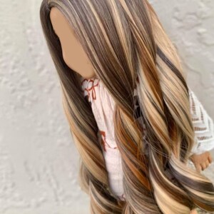 May include: Long, wavy doll hair wig with brown, blonde, and light brown streaks. The wig is styled in a side part with loose waves.
