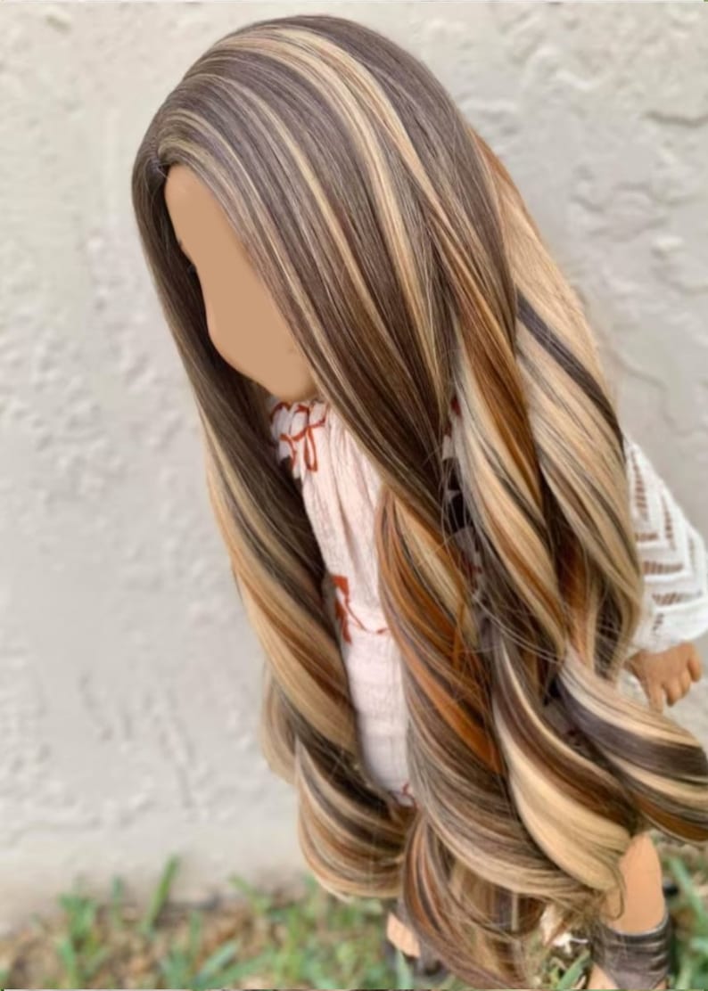 May include: Long, wavy doll hair wig with brown, blonde, and light brown streaks. The wig is styled in a side part with loose waves.