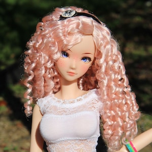May include: A doll with long, curly, pink hair wearing a white lace top and a black headband with a spider charm.