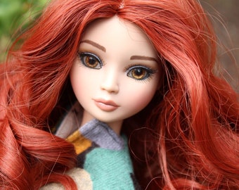 May include: A red-haired doll with blue eyes and a light blue, green, and yellow patterned shirt.