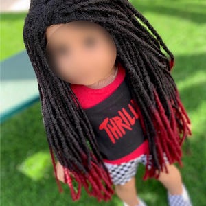 May include: A doll with black dreadlocks that fade to red at the ends. The doll is wearing a red and black shirt with the word "THRILL" in red, checkered shorts, and grey and white checkered slip-on shoes.