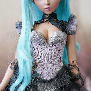 Puede incluir: Una mu&ntilde;eca con el pelo largo y azul claro que lleva un cors&eacute; negro y plateado con detalles de encaje. La mu&ntilde;eca tiene ojos azules y una cara delicada.