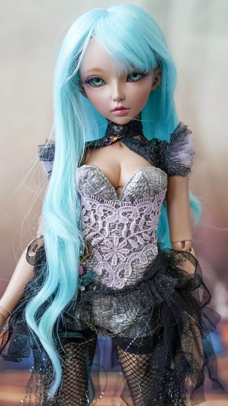 Puede incluir: Una mu&ntilde;eca con el pelo largo y azul claro que lleva un cors&eacute; negro y plateado con detalles de encaje. La mu&ntilde;eca tiene ojos azules y una cara delicada.