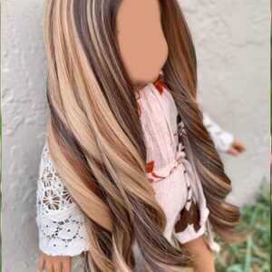 May include: A long, wavy doll wig with brown, blonde, and light brown streaks. The wig is styled in a side part and has a natural, flowing look.