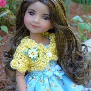 May include: A doll with long brown hair wearing a yellow crocheted shrug over a blue and white floral dress.