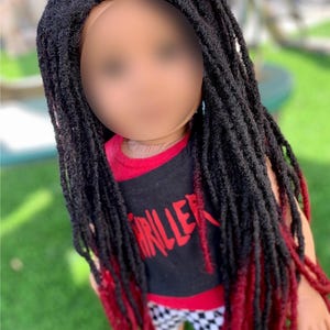 May include: A doll with a black and red wig featuring long dreadlocks. The doll is dressed in a black tank top with the word "THRILLER" in red and checkered shorts. The dreadlocks are tipped with red.