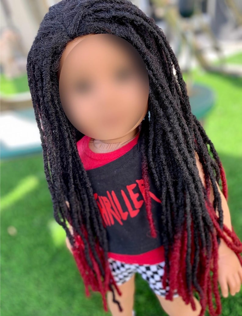 May include: A doll with a black and red wig featuring long dreadlocks. The doll is dressed in a black tank top with the word "THRILLER" in red and checkered shorts. The dreadlocks are tipped with red.
