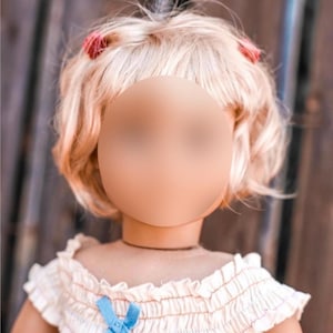 Può includere: Una bambola con i capelli biondi acconciati a caschetto con due fermagli rossi. La bambola indossa un vestito bianco senza spalline con un nastro blu.