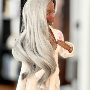 May include: A doll with long, silver-grey hair wearing a white, silky robe with a pink floral design.