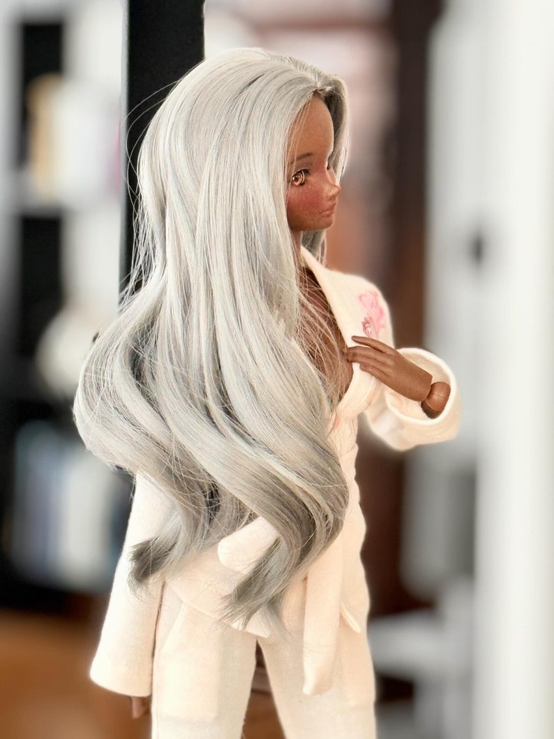 May include: A doll with long, silver-grey hair wearing a white, silky robe with a pink floral design.