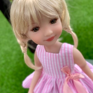 May include: A blonde doll with green eyes wearing a pink and white striped dress with a pink bow.